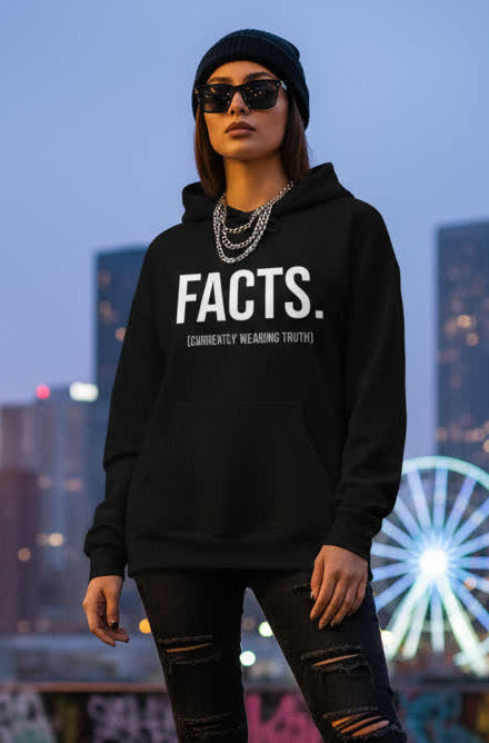 Person wearing a black hoodie with 'FACTS.' text in an urban setting with a ferris wheel.